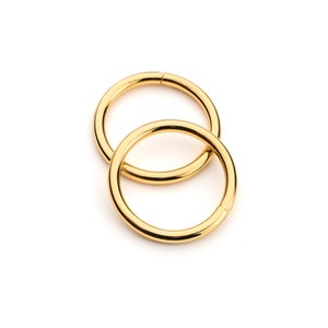 May include: Two gold-colored metal rings, one slightly larger than the other, are interlocked. The rings are smooth and shiny.