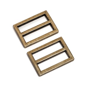 May include: Two antique gold metal slider buckles. The buckles are rectangular with two parallel slots.