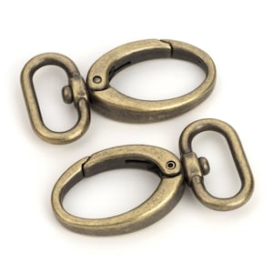 May include: Two antique gold-toned metal swivel clasps with oval rings. The clasps are closed and ready to be attached to a bag, purse, or other item.