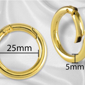 May include: Two gold-colored metal key rings with a spring-loaded clasp. The larger ring measures 25 mm in diameter and the smaller ring measures 5 mm in diameter.