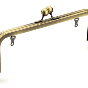May include: An antique brass-toned purse frame with a curved rectangular shape. The frame features a double ball clasp and small loops for attaching fabric. The metal has a slightly aged appearance, suggesting a vintage or handcrafted item.