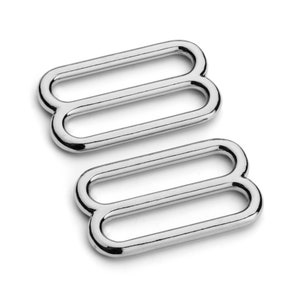 May include: Two shiny, silver-colored metal sliders. Each slider has three parallel, rectangular loops connected by curved ends, creating a figure-eight shape. The objects are set against a white background, with a slight shadow.