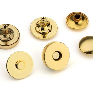 May include: Six gold-toned metal snap fasteners, some with a raised center, others with a flat surface. These are used for clothing or crafts.