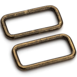 May include: Two antique gold metal D-rings. The rings are rectangular in shape and have a smooth, slightly textured surface.