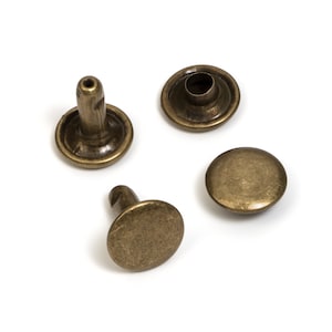 May include: Four antique brass rivets, each with a rounded cap and a post. The rivets are a warm, metallic color, and are designed for use in leathercraft, garment construction, or other crafting projects. The rivets are shown against a white background.