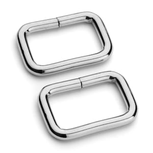 May include: Two silver metal D-rings, each with a smooth, rounded surface. The rings are approximately 1 inch in diameter.