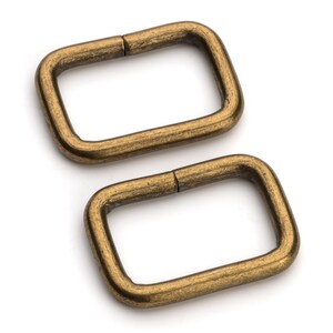 May include: Two antique gold-toned metal D-rings. The rings are rectangular in shape with rounded corners.