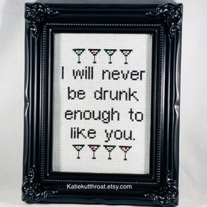 May include: A framed cross-stitch with the text "I will never be drunk enough to like you."  The text is surrounded by five green, red, and white martini glasses.