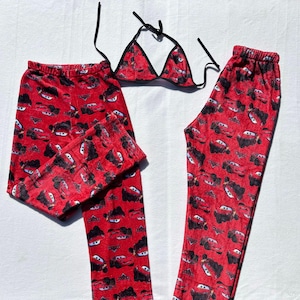 May include: A red pajama set with a pattern of black and white cartoon cars. The set includes pajama trousers and a matching triangle bikini top with black trim and ties. The fabric appears soft and plush.