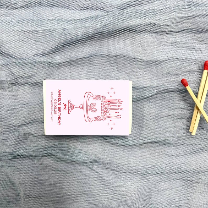 May include: A white matchbox with a red illustration of a birthday cake with candles and the text "Angel's Birthday 05.03.25 123 Anywhere St, Any City"