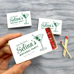 May include: White matchboxes with green text and a martini glass illustration. The text reads "Stole this from... Selina's BIRTHDAY PARTY Best party in town." One box is open, revealing red match heads. Two loose matches are visible.