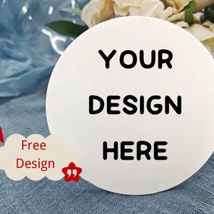 May include: A white, circular product with the text "YOUR DESIGN HERE" in bold black letters. A small, cream-coloured cloud-shaped graphic with the words "Free Design" is on the left. The background includes blue fabric and flowers.