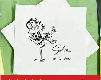 May include: White cocktail napkin with a black and white illustration of a woman in a martini glass, wearing a cowboy hat and boots. The name "Selina" and the date "10-10-2030" are printed below the illustration. The napkin is on a green surface.