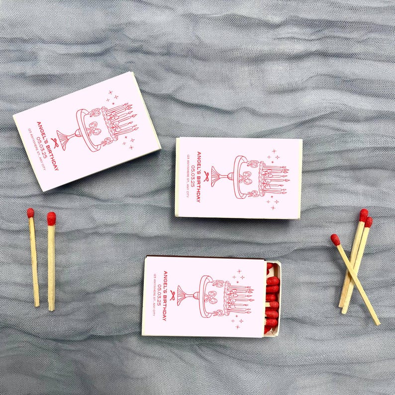 May include: Three matchboxes with pink and white labels. The labels have a red illustration of a cake with candles and the text "Angel's Birthday 03.03.23".