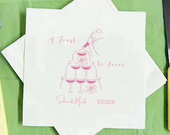 May include: White paper napkin with a pink illustration of champagne glasses stacked in a pyramid, with the text "A Toast to Forever". The names "Selina & Mark" and the date "10.10.2030" are also printed on the napkin.