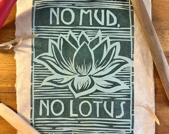 May include: A teal and white linocut print on textured paper. The print features a lotus flower and the text "NO MUD, NO LOTUS." Printmaking tools, including a brayer and a wooden burnisher, are visible.