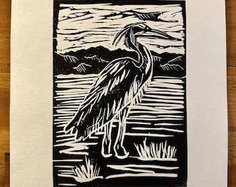 May include: Black and white woodcut print of a heron standing in a marsh. The print is signed "Mary Slat" and numbered "1/5".
