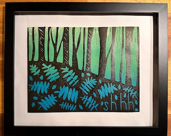 May include: Framed art print featuring a forest scene in shades of green and blue on a black background. The print includes stylized trees and foliage, with the word "shhh" at the bottom. The artwork is encased in a black frame.