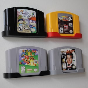 May include: Four Nintendo 64 game cartridges in black and gray holders. Games include Rugrats, Tony Hawk's Pro Skater 2, Super Mario 64, and 007 GoldenEye. The cartridges are in various colors, including black, yellow, and gray.
