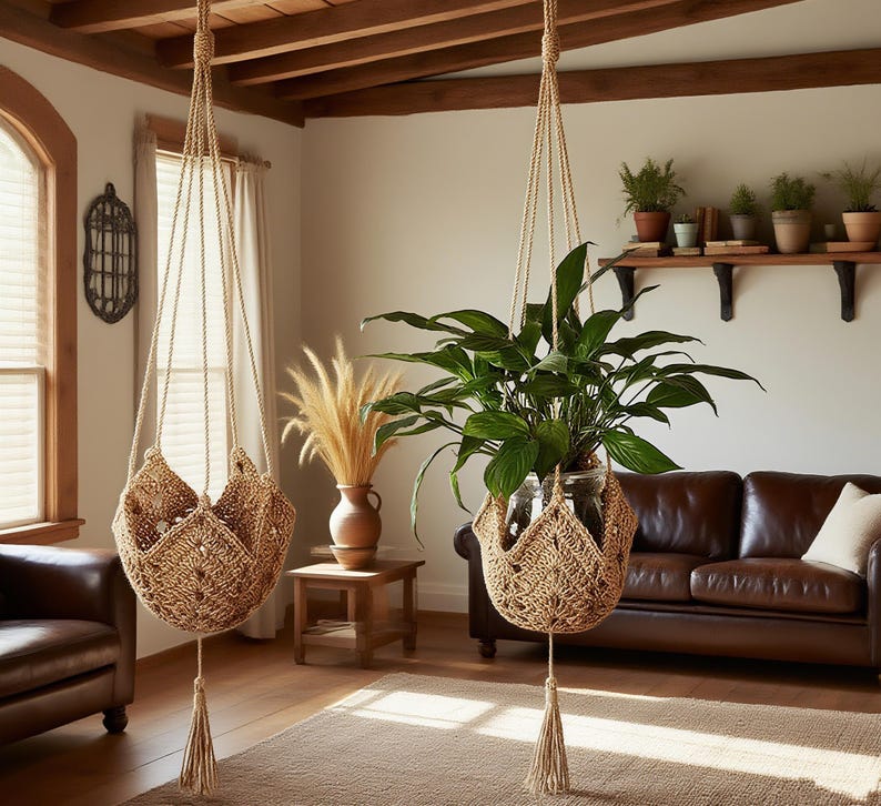 May include: Two hanging macrame plant holders with plants inside. The holders are a light brown color and have a woven design. The plants have green leaves and are in clear glass containers. A brown leather sofa is in the background.