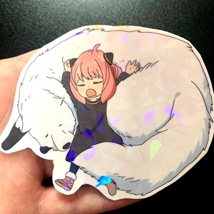May include: A sticker featuring a cartoon girl with pink hair sleeping on a white furry animal. The sticker has a holographic finish.