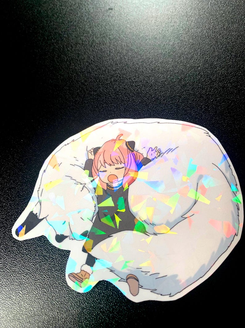 May include: A sticker featuring a cartoon girl with pink hair and a black dress, sleeping on a large white furry animal with iridescent glitter.