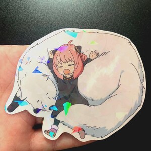 May include: A sticker featuring a cartoon girl with pink hair sleeping on a white fluffy animal. The sticker has a holographic finish.