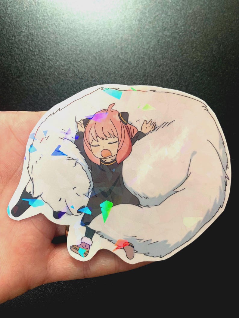 May include: A sticker featuring a cartoon girl with pink hair sleeping on a white fluffy animal. The sticker has a holographic finish.