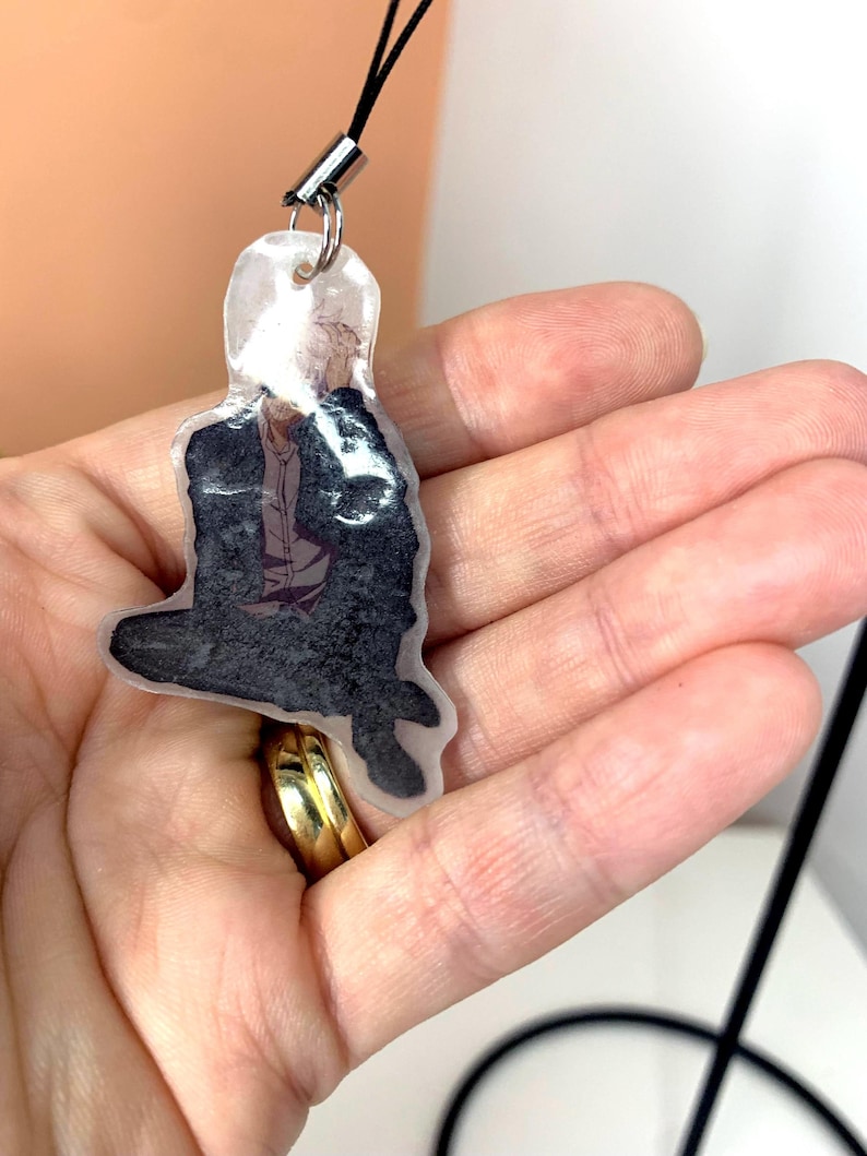 May include: A clear plastic keychain with a black and white image of a person sitting down. The keychain has a black string attached to it.