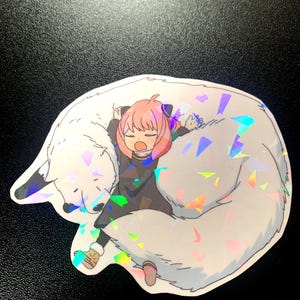 May include: A holographic sticker featuring a pink-haired anime character sleeping on a white wolf. The sticker has a sparkly, iridescent finish.