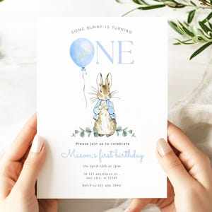 May include: A blue and white invitation card with a Peter Rabbit illustration. The card says "Some bunny is turning one" and includes details for a first birthday party.