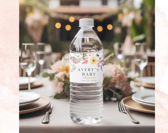 Könnte beinhalten: Eine transparente Plastikwasserflasche mit weißem Deckel und einem Etikett mit der Aufschrift "Avery's Baby Shower". Das Etikett ist mit bunten floralen Designs verziert. Die Flasche steht auf einem Tisch, der für eine Party gedeckt ist.