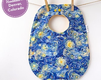 May include: A blue and yellow baby bib with a starry night design. The bib has a yellow snap closure and is handmade in Denver, Colorado.