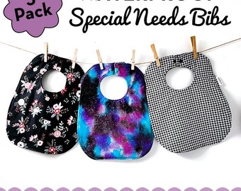 May include: Three waterproof Special Needs bibs hanging on a clothesline. One bib is black with a floral pattern, another has a blue and purple galaxy design, and the third is black and white houndstooth. The text reads "WATERPROOF Special Needs Bibs" and "3 Pack".