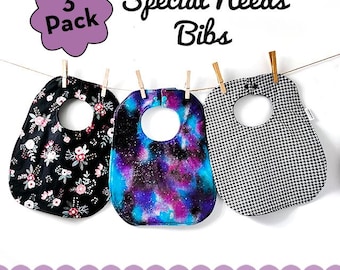 May include: Three pack of special needs bibs hanging on a clothesline. The bibs are made of different fabrics, including a black floral print, a blue and purple galaxy print, and a black and white houndstooth print. The text "Special Needs Bibs" is written above the bibs. The text "3 Pack" is written in a purple cloud shape. The text "45+ Fabric Choices. Fits age 8+" is written below the bibs.