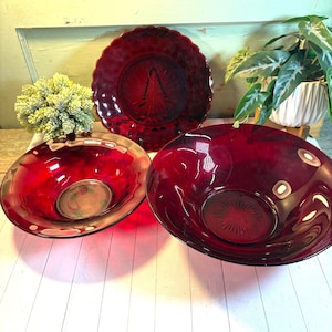 以下が含まれることがあります： ルビーレッドのガラス食器3点セット。楕円形のボウル2つと、スカラップエッジの丸いプレートが含まれています。プレートはテクスチャード加工された表面と中央のデザインが特徴です。ボウルは滑らかな内側を持っています。