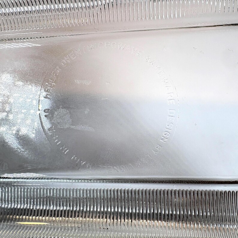 May include: Close-up of a clear glass object with a textured surface. The object has a circular marking with the text "HELLER OVEN/MICRO WAYS" and "SAFE DESIGN BY L.B. LIGNE".