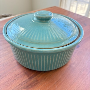 May include: A teal blue ceramic casserole dish with a lid. The dish has a ribbed design and the lid has a knob on top.