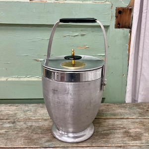 Op de afbeelding: Een zilveren ijs emmer met een zwarte handgreep en een gouden deksel met een zwarte knop. De emmer heeft een getextureerd oppervlak en een ronde basis.