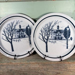 Pode incluir: Dois pratos de jantar de cerâmica branca com uma borda azul e uma ilustração em preto e branco de uma escola com árvores e crianças brincando na frente.
