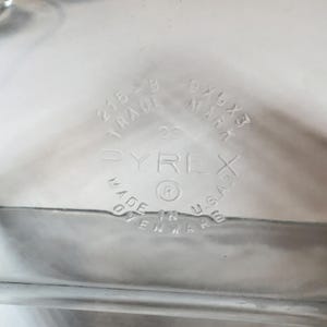 May include: Clear Pyrex baking dish with embossed text. The text includes "PYREX", "MADE IN U.S.A.", and dimensions "9x5x3". The dish also has the numbers "215-B" and "22".