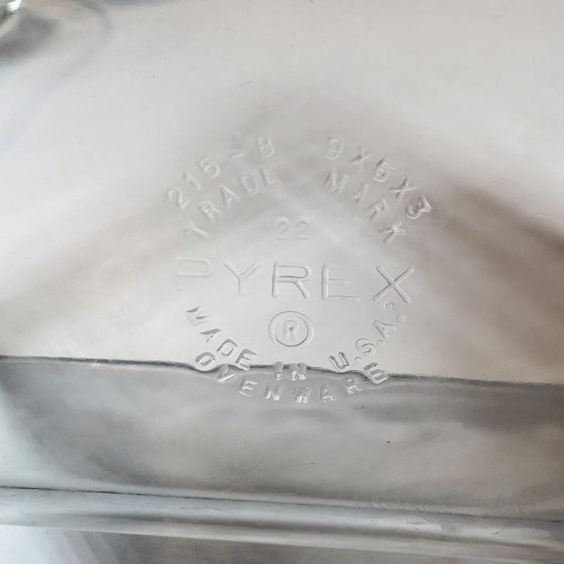 May include: Clear Pyrex baking dish with embossed text. The text includes "PYREX", "MADE IN U.S.A.", and dimensions "9x5x3". The dish also has the numbers "215-B" and "22".
