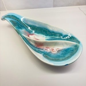 Könnte beinhalten: Eine Keramik-Servierplatte mit einem einzigartigen wellenförmigen Design. Die Platte ist in Blautönen, Grün- und Weißtönen mit rosa Akzenten glasiert.