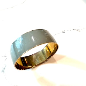 Op de afbeelding: Een brede, grijze emaille armband met een goudkleurig interieur. De armband heeft een gladde, glanzende afwerking en een eenvoudig, modern design. Dit sieraad is geschikt voor dagelijks gebruik.