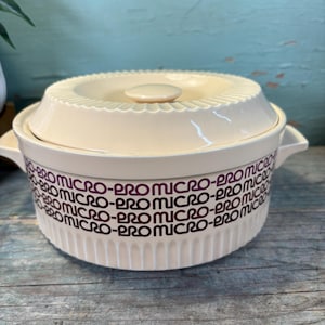 以下が含まれることがあります： クリーム色のセラミックキャセロール皿と蓋。 皿はリブ付きの外観とハンドルが付いています。 「PROMICRO」の文字が濃い紫色の繰り返し模様で印刷されています。 蓋には小さなノブが付いています。