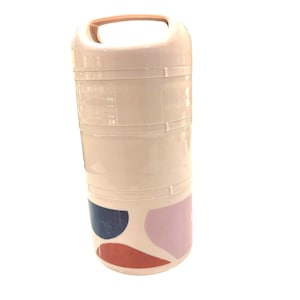 May include: A stacked, light pink lunch container with a handle. The container has three sections and is decorated with abstract shapes in navy blue, pink, and rust-orange. The handle is a lighter shade of pink.