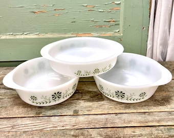 May include: Three white ceramic baking dishes with green floral designs. The dishes are stacked on top of each other on a wooden surface.