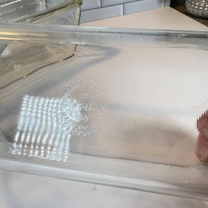 May include: Clear glass Pyrex loaf pan. The pan has a rectangular shape with rounded corners. The Pyrex logo and text are embossed on the side. The pan is clean and appears to be unused.