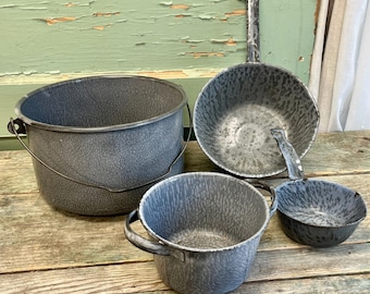 May include: Set of four gray enamelware kitchenware pieces, including a large pot with a handle, a medium-sized bowl, a smaller bowl, and a small cup. The pieces are all made of gray enamelware with a speckled finish.