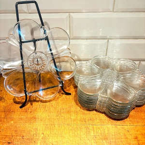 Puede incluir: Dos platos de servir de vidrio transparente con forma de flor. Un plato está en un soporte negro y el otro está apilado sobre sí mismo.